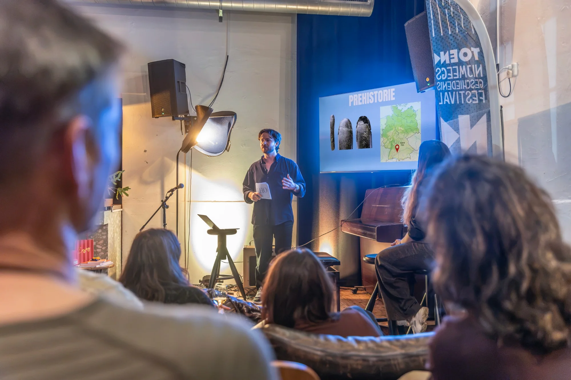 Justus Luijckx geeft een lezing voor publiek tijdens het Nijmeegs Geschiedenisfestival TOEN, met een dia over prehistorie op het scherm